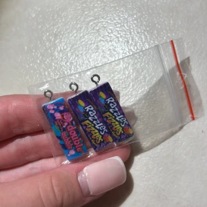 Godis berlocker i lila och blått - Tre rektangulära örhänges berlocker med godistema, två med lila Razzles Fizzles-motiv och ett med blått Double Bubble-motiv. Färgglada och lekfulla, perfekta för dig som gillar unika accessoarer med en twist av nostalgi.