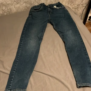 Blå jeans från Lindex, storlek 164 - Snygga blå jeans från Lindex i storlek 164. Klassisk femficksmodell med normal passform och raka ben. Jeansen har en lätt tvättad look och är tillverkade i mjukt bomullsmaterial. Perfekta för en avslappnad stil.
