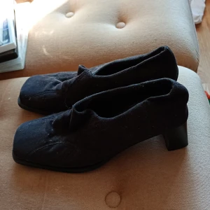 Svarta pumps med låg klack - Stilrena svarta pumps med fyrkantig tå och låg klack. Skorna har en enkel design i mjukt tygmaterial och passar perfekt till dig som gillar klassiska och minimalistiska skor.