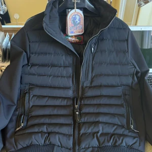 Svart pufferjacka från Parajumpers - Snygg svart pufferjacka från Parajumpers med quiltad framsida, ribbade muddar och dragkedjor på fickorna. Jackan har hög krage och klassisk logga i nacken. Perfekt för dig som vill ha en stilren och sportig look.