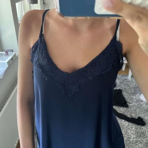 Mörkblå linnetopp med spetsdetaljer - Supersnygg mörkblå linnetopp med tunna axelband och v-ringning. Toppen har fina spetsdetaljer längs ringningen som ger en extra touch. 💕