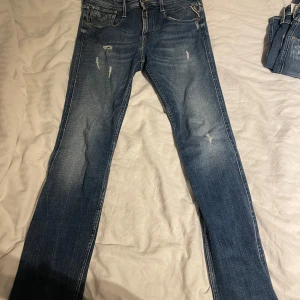 Blå Replay jeans i rak modell - Snygga blå jeans från Replay i rak passform med slitna detaljer framtill. Klassisk femficksmodell med läderpatch bak i midjan. Tillverkade i hållbar bomull för en schysstare stil. Perfekta till sneakers och hoodie.