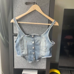Jeanskorsett topp från Weekday - Säljer en snygg croppad jeanskorsett från Weekday i klassisk blå denim. knappar framtill för en cool look