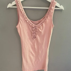 Ljusrosa linnetopp med volangdetaljer - Supersöt ljusrosa linnetopp med volangkant längs urringningen och knappar framtill.   OBS!! den är omsydd från M till XS och kommer ha tecken på att den är sydd hemma. Fortfarande i fint skick 🤍