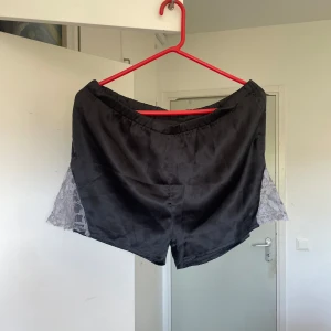 Svarta silkes-shorts med spetsdetaljer - Svarta shorts i silkesliknande material med grå spets på sidorna. De har en loose passform, midjan är inte så elastisk