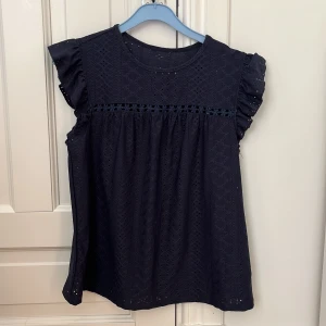 Mörkblå blus  - En jättefin mörkblå blus med fina detaljer som blommor och hål. Den har volanger på ärmarna och den är tun och i ett väldigt skönt material passar jätte bra en varm sommardag med ett par jeans eller en kjol!