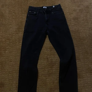 Svarta jeans från Jack & Jones - Säljer ett par svarta jeans från Jack & Jones med klassisk femficksdesign och raka ben. Jeansen har en stilren look och är tillverkade i ett mjukt denimtyg som sitter snyggt. Perfekta för dig som gillar en enkel och clean stil.