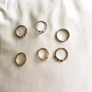 6 stycken tunna ringar i guld  - Säljer ett set med sex tunna ringar i guldfärgad . Några ringar har små stenar och detaljer, en har ett hjärta och andra är enkla och släta. Ingen är använd förutom den med hjärtat som är lite uttvättad dom andra är som nya. (inte äkta guld)