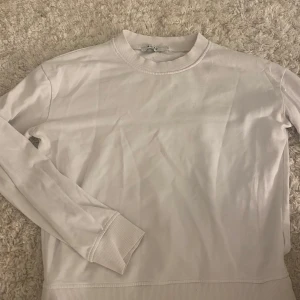 Vit sweatshirt från NA-KD - En stilren vit sweatshirt från NA-KD i storlek S. Tröjan har rund halsringning, långa ärmar och ribbade muddar vid ärmslut och nederkant. Perfekt för en clean och enkel look. Tillverkad i mjuk bomull för skön komfort.