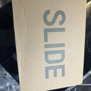 Adidas Yeezy Slide i beige strl 39-40 - Säljer ett par Adidas Yeezy Slide i beige färg. De har en chunky, vågig sula och är tillverkade i syntetmaterial. Perfekta för en avslappnad stil och riktigt bekväma att glida runt i.