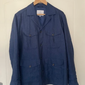 Blå linnéjacka från Bläck - Säljer en stilren blå linnéjacka från Bläck med fyra fickor framtill och knäppning med knappar. Jackan har klassisk krage och lång ärm, perfekt för vår och sommar. Enkel och snygg design som passar till mycket. Nypris 1300kr. 