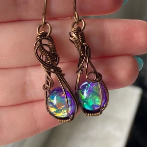 Handgjorda örhängen med pärlor med ”opaleffekt” och koppartråd. Reserverad!✨ - Unika örhängen med skimrande regnbågsfärgade pärlor infattade i konstnärligt snirklad koppartråd. Färgerna skiftar i grönt, lila, gult och blått beroende på ljuset. Perfekta för dig som vill sticka ut med ett färgglatt smycke.