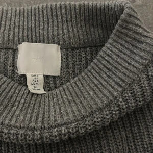 Gråvit randig stickad tröja från H&M - Superfin stickad tröja från H&M i grått med vita horisontella ränder. Tröjan har en croppad passform, rund halsringning och långa ärmar. Perfekt för lager-på-lager och enkel att styla till olika outfits. Tröjan har använts fåtal gånger och är i väldigt bra skick! 