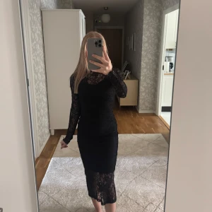 Svart spetsklänning med lång ärm Stockh LM - Säljer en elegant svart klänning i spets med lång ärm och figurnära passform. Klänningen har en hög halsringning och är helfodrad förutom vid ärmarna där spetsen är genomskinlig. Perfekt för dig som vill ha en klassisk och stilren look.