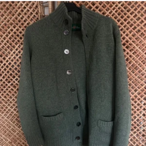 Grön Alan Paine Kofta - Mysig grön Alan Paine kofta med hög krage och stora knappar framtill. Två fickor framtill och ribbade muddar vid ärmslut och nederkant. Perfekt för lager-på-lager och enkel att matcha med olika outfits. Nypris: 2500kr | Pris: 1099kr! 