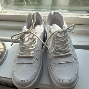 Vita sneakers med platåsula - Säljer ett par fräscha vita sneakers med platåsula och snörning. Skorna har detaljer på sidorna och en rund tå. Perfekta för dig som vill ha en stilren och modern look. Enbart testade men tyvärr för små för mig