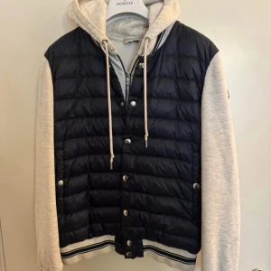 Svart pufferjacka med grå luvärm från Moncler - Snygg blå/grå cardigan från Moncler. Perfekt för vår, höst och sommar. Retail 8.000kr