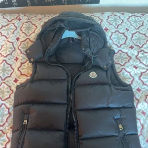 Moncler väst (A-koppia) - Snygg moncler väst i underbart skick även med luva perfekt med en t shirt under nu till sommar och speciellt med luva för man vet aldrig när det kan börja regna😉