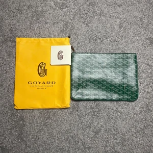  G|oyard dator fodral / necesär grön - Säljer en grön kuvertväska från G|oyaed med klassiskt mönster och dragkedja upptill. Väskan är tillverkad i skinn och har G|oyard ikoniska logga tryckt på framsidan. Perfekt accessoar för att bära det viktigaste med stil.  Inte äkta!!!!