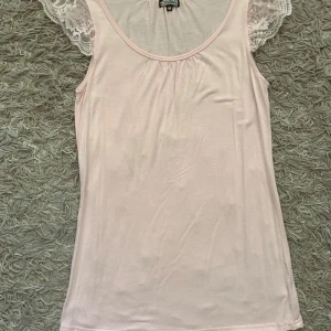 Ljusrosa topp med spetsärmar från Little Boho - Supersöt ljusrosa topp från Little Boho med ärmlösa spetsärmar i blommigt mönster. Mjuk och tunn bomullskänsla, perfekt för sommardagar. Rund halsringning och romantisk vibe. Säljes i storlek S.