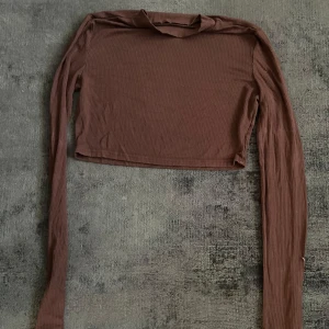 Brun croppad långärmad topp - Säljer en brun croppad långärmad topp med ribbad struktur. Perfekt för att styla med höga jeans eller kjol. Enkel och stilren design som passar till många olika looks.