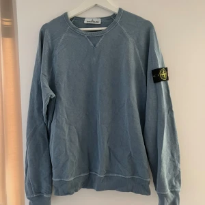 Blå sweatshirt från Stone Island - Säljer en blå sweatshirt från Stone Island med klassisk patch på vänster ärm. Tröjan har rund halsringning och långa ärmar. Perfekt för en avslappnad och stilren look.
