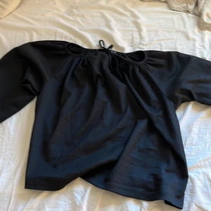 Svart blus med knytning i halsen - Säljer en svart blus med lång ärm och knytning vid halsen. Blusen har en lös passform och är perfekt för en stilren look. Materialet känns lätt och luftigt.