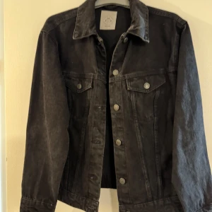 Svart jeansjacka Vero Moda - Klassisk svart jeansjacka med knappar framtill och två bröstfickor med lock. Jackan har en rak passform och krage, perfekt för en avslappnad stil. Passar till många olika outfits och är ett tidlöst plagg i garderoben.