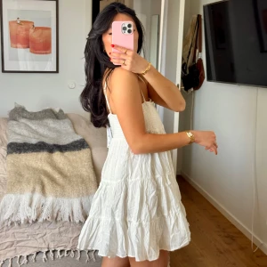 Vit somrig klänning med smock och volanger - Säljer denna såå söta vita slutsålda klänningen från Zara med smockad överdel och volangig kjol. Klänningen är väldigt kort och slutar ca mitten på låren på mig, jag är 160 cm lång. Endast provad på och aldrig använd, prislappen fortfarande på🌻