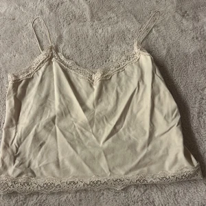 Beige linnetopp med spets från ONLY - Säljer en söt beige linnetopp från ONLY med tunna axelband och fina spetsdetaljer längs halsringning och nederkant. Säljer den då den inte kommer till användning använd max 2 gånger priset går att diskutera💗💗