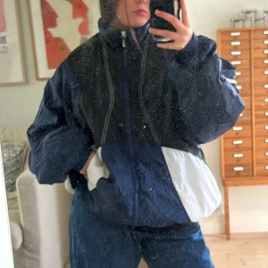 Blå och vit vindjacka från Nike - Säljer en blå och vit vindjacka från Nike med dragkedja och hög krage. Jackan har en oversized passform och klassisk Nike-logga på ärmen.