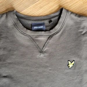 Olivgrön sweatshirt från Lyle & Scott Small - Säljer en mörk olivgrön sweatshirt från Lyle & Scott med klassisk rund hals och original logga på bröstet. Storlek Small. Tröjan har långa ärmar och ribbade muddar vid ärmslut och nederkant. Använd enbart 2-3ggr innan sonen växte ur den, så mycket fint skick! Hämtas i Huskvarna vid överenskommelse eller skickas.