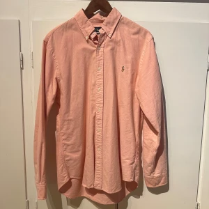 Ljusrosa skjorta från Ralph Lauren - Säljer en ljusrosa skjorta från Ralph Lauren i slim fit-modell. Skjortan har klassisk krage, knappar framtill och broderad logga på bröstet. Perfekt för dig som gillar stilrena och tidlösa plagg.