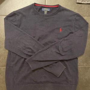 Marinblå tröja från Ralph Lauren - Säljer en Marinblå tröja från Ralph Lauren i mjuk pima bomull. Tröjan har en röd broderad logotyp på bröstet och ribbade kanter. Perfekt för en stilren look. Tröjan är XL i barn storlek som sitter som Xs. Skulle rekommendera att köpa tröjan om du har storlek xs då jag själv har xs och den sitter perfekt🤩