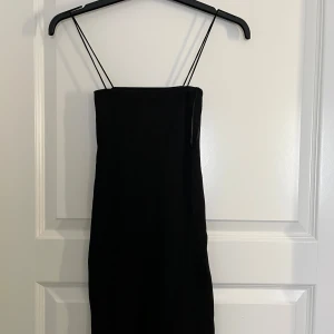Svart axelbandslös klänning från Zara - Säljer en svart, tight klänning från Zara med tunna axelband. Klänningen har en minimalistisk design och är perfekt för dig som gillar en stilren look. Passar dig som vill ha en enkel men snygg outfit.
