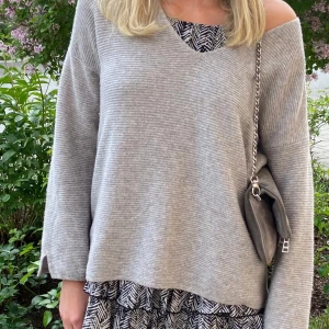 Grå ribbad stickad tröja från United Colors of Benetton - Mysig grå stickad tröja med ribbad struktur och v-ringning från United Colors of Benetton. Tröjan har lång ärm och en avslappnad passform. 