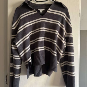 Randig v-ringad tröja från AWARE - Mörkgrå v-ringad tröja från AWARE med vita ränder. Tröjan har långa ärmar och en lös, asymmetrisk passform.💕