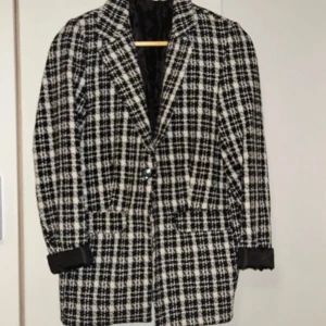Svartvit rutig kavaj - Säljer en svartvit rutig kavaj med klassiskt snitt och långa ärmar. Kavajen har knäppning framtill och är helfodrad med svart innerfoder. Perfekt för en stilren och trendig look.