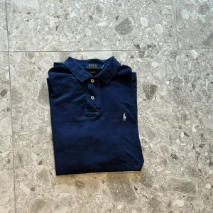 Mörkblå pikétröja från Polo Ralph Lauren - Säljer en klassisk mörkblå pikétröja från Polo Ralph Lauren. Gjord av bomull och nypriset på denna är cirka 1600kr