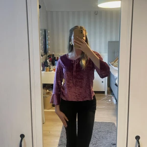 Lila sammetsblus med knyt från Bo Company - Säljer en lila sammetsblus från Bo Company med v-ringning och knyt framtill. Blusen har medel-långa ärmar med lätt volang vid ärmslut och en glansig finish som ger en lyxig känsla. Perfekt för dig som vill sticka ut med färg och material!