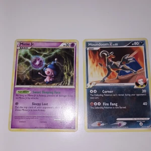Pokémonkort Mime Jr. och Houndoom - Två samlarkort från Pokémon: Mime Jr. (psykisk typ) och Houndoom (mörk/eld typ). Mime Jr. har lila och gröna färger med en tecknad figur, medan Houndoom har en mörk bakgrund med eld och en hundliknande Pokémon. Båda korten har klassisk Pokémon-design.