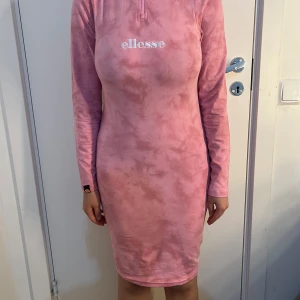 Rosa långärmad klänning från Ellesse - Säljer en rosa långärmad klänning från Ellesse med broderad logga framtill. Klänningen har en tight passform och är tillverkad i mjuk, stretchig syntet. Perfekt för dig som gillar sportig och bekväm stil.