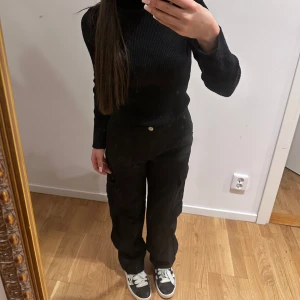 Svarta cargopants med raka ben - Svarta cargopants med raka ben och flera fickor på sidorna. Byxorna har normal passform och stängs med knapp och dragkedja. 