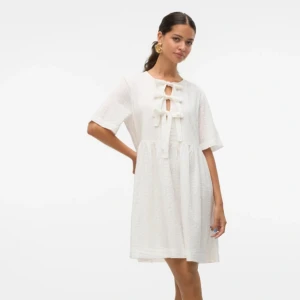 Vit kortklänning med knyt och broderade detaljer från H&M - Superfin vit kortklänning från med broderade detaljer och tre knyt framtill. Klänningen har korta ärmar och en avslappnad passform.  Söt och trendig modell som passar till många tillfällen som till exempel studenten!! Passar S-M. Helt ny med prislapparna kvar!!