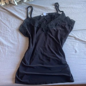 Svart spetsklänning från Amisu - Säljer en svart kortklänning från Amisu med smala axelband och v-ringad spetsdetalj upptill. Klänningen har en slimmad passform och är perfekt för dig som gillar en enkel men elegant stil.