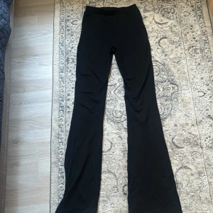 Svarta utsvängda byxor i bomull - Svarta byxor med utsvängda ben och hög midja. Tillverkade i mjukt bomullsmaterial, perfekta för en stilren och bekväm look. Passar dig som gillar en klassisk och enkel stil.