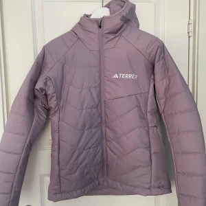 Ljuslila pufferjacka från Adidas Terrex - Säljer en helt ny ljuslila pufferjacka från Adidas Terrex med huva och dragkedja framtill. Jackan har lång ärm och en sportig look, perfekt för kyliga dagar. Adidas Terrex-logga på bröstet. Snygg och funktionell jacka för dig som gillar outdoor. Den är i storlek s. Hur av dig om du har några funderingar, pris kan diskuteras.