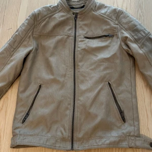 Beige jacka - Beige jacka från Jack and Jones med ståkrage och dragkedja framtill. Jackan har tre fickor med dragkedja och diskreta sömdetaljer på axlarna. Säljs för 300kr. 
