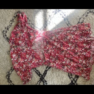 Röd blommig kortklänning med öppen rygg - Säljer en röd kortklänning med blommigt mönster och volangdetaljer. Klänningen har korta puffärmar, markerad midja och en snygg öppen rygg. Perfekt för sommarens alla tillfällen! Storleken är 40 men är 36a och den passar fint