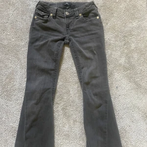 Svarta jeansbyxor från True Religion - Intressekoll på ett par svarta True Religion jeans, modell Jow Low Rise Flare. Byxorna har klassiska detaljer med synliga sömmar, knappar med logga och fickor både fram och bak. Flare-modell med låg midja och snygg passform.